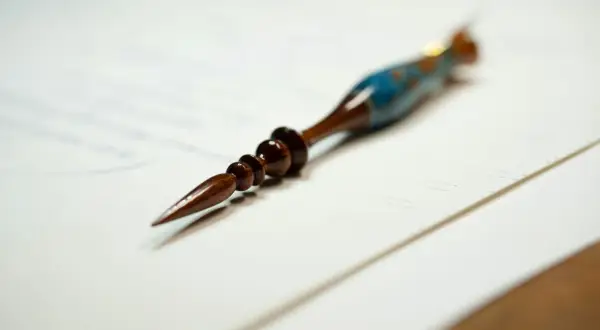 Eleganckie pióro do kaligrafii, ozdobione niebieskimi i złotymi detalami, leży na papierze. Może posłużyć do stworzenia dzieła sztuki, zgodnie z art. 63 kp.