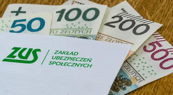 Koperta ZUS z logo i napisem "Zakład Ubezpieczeń Społecznych" na tle polskich banknotów 50, 100, 200 i 500 zł. Symbolizuje świadczenie kompensacyjne.