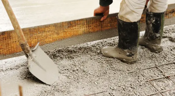 Pracownik w gumowcach układa szalunek do fundamentów. Widać łopatę i świeży beton. Jaki cement na fundamenty?
