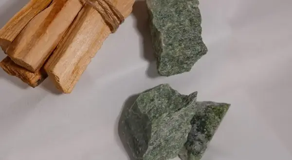 Surowe kawałki jadeitu w odcieniach zieleni, obok wiązki drewna Palo Santo.