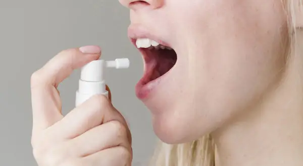 Persona aplica spray bucal con gluconato de clorhexidina para aliviar el dolor de garganta.