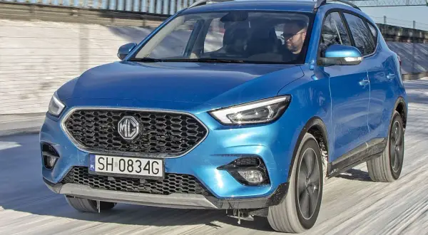 Niebieski MG ZS Classic jedzie po zaśnieżonej drodze. Kierowca w okularach prowadzi auto.