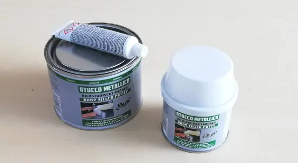 Due barattoli di stucco metallico, uno aperto con un tubetto di indurente sopra. Pronto per riparare metalli.