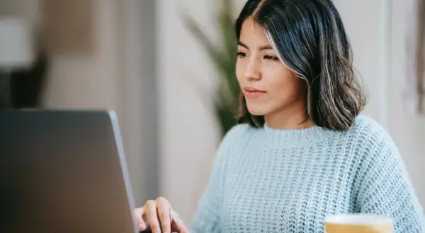 Junge Frau schreibt am Laptop eine Rechnung als Privatperson. Sie trägt einen hellblauen Strickpullover.