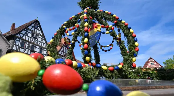 Bunte Ostereier schmücken einen Tannenkranz vor Fachwerkhäusern. Es gibt Karsamstag, die Vorfreude auf Ostern ist spürbar.