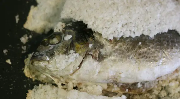 Dorada a la sal, lista para hornear. El pescado está cubierto de sal gruesa, con su cabeza visible.