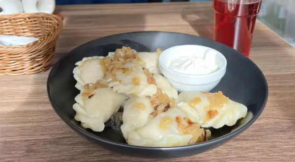Leckeres Essen in Breslau: Dampfende Pierogi mit Zwiebeln und Sauerrahm, dazu ein rotes Getränk.