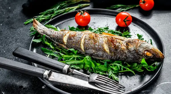 Un bar au four, doré et savoureux, servi sur un lit de roquette avec des tomates cerises et des herbes. Un plat simple et élégant.