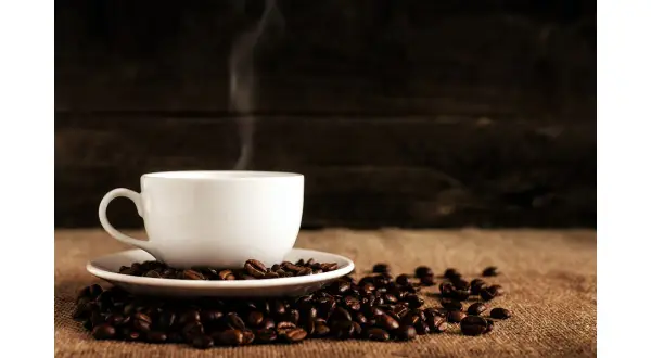 En vit kopp med ångande kaffe står på en hög med kaffebönor. Hur många koppar kaffe per dag är din gräns?