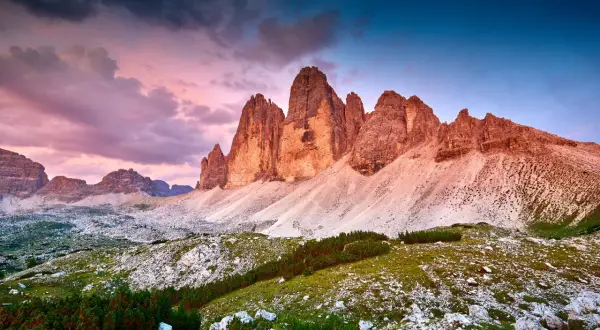 Le maestose cime di Lavaredo illuminate dal tramonto, con un cielo viola e blu che fa da sfondo a un paesaggio alpino mozzafiato.