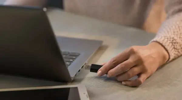 Dłoń próbuje podłączyć pendrive do laptopa, ale komputer widzi pendrive ale go nie czyta.