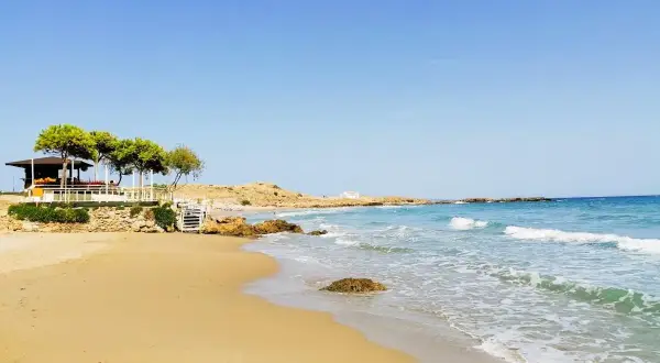 Piękne zakynthos plaże z piaszczystym brzegiem, turkusową wodą i kamienistymi wysepkami. W oddali widać biały domek i zielone drzewa.