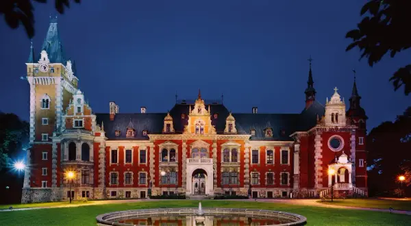 Pałac w Pławniowicach nocą, z oświetloną fasadą i wieżą zegarową. Wspaniałe pławniowice atrakcje czekają na zwiedzających.
