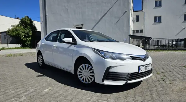 Biała Toyota Corolla 2017 zaparkowana na placu przed budynkiem.