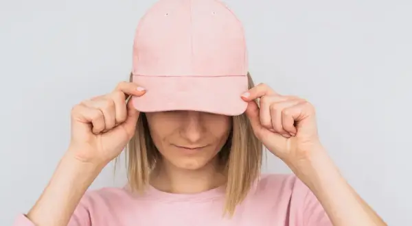 Frau mit rosa Cap, die sie mit beiden Händen vor die Augen hält. Sie zeigt, wie man eine Cap richtig tragen kann.