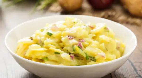 Omas Kartoffelsalat in einer Schüssel, mit Zwiebeln und Schnittlauch, auf einem Holztisch.