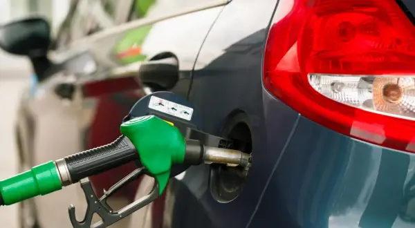 Grön bensinpump fyller på en mörkblå bil. Tänk på din bensin per km för att köra smartare.