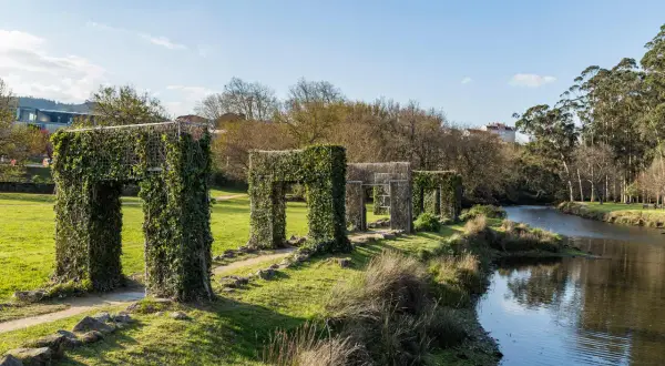 Paseo por la illa das esculturas Pontevedra, con arcos cubiertos de hiedra junto a un río.