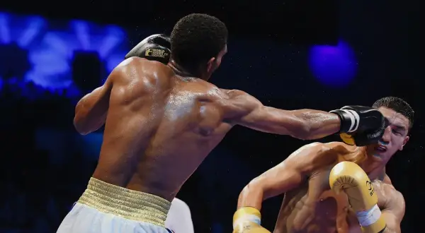 A boxer lands a punch, sweat flying, as the crowd awaits the boxing decisions.