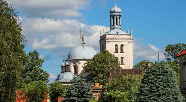 Majestatyczna fara w Grodzisku Wlkp. z kopułą i wieżą, otoczona zielenią drzew.