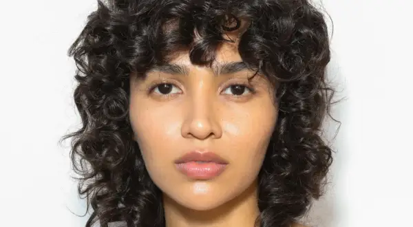 Volto di donna con capelli ricci scuri e un audace taglio capelli anni 80 mullet.