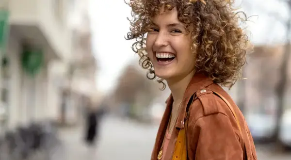 Frau mit vollen, lockigen Haaren, die lacht. Perfekt gestylte Locken, die ihr Gesicht umrahmen.