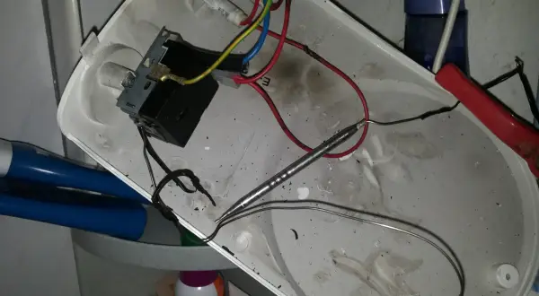 Rozmontowany bojler z widocznym termostatem i przewodami. Jak sprawdzić termostat w bojlerze? To zdjęcie pokazuje wnętrze, gdzie znajduje się element grzewczy i okablowanie.