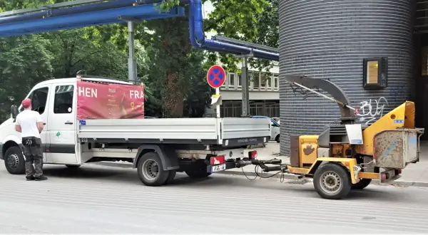 Ein Handwerker steht neben einem LKW mit Anhänger, der einen Holzhäcksler transportiert.