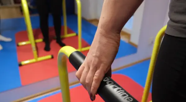 Rehabilitacja po niedowładzie nóg: ćwiczenia na poręczach. Dłoń trzymająca uchwyt.