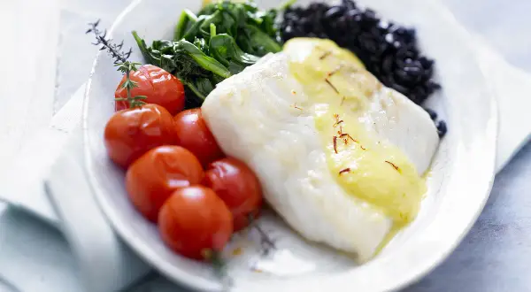 Filet de poisson blanc nappé de sauce safranée, accompagné de tomates cerises rôties, d'épinards et de riz noir. Une belle recette de turbot.