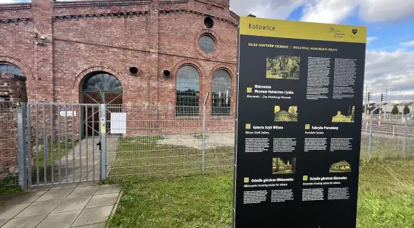 Tablica informacyjna Szlaku Zabytków Techniki w Katowicach, obok ceglanej budowli dawnej huty.