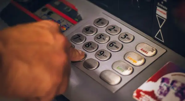 Dłoń wpisuje PIN na klawiaturze wpłatomatu bez karty.