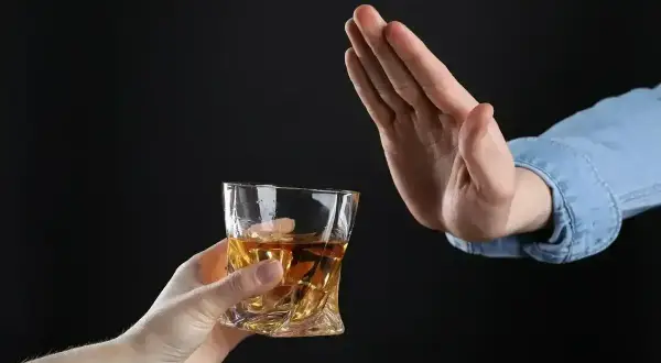 Ręka odrzuca szklankę z alkoholem. Czy dzień przed wyrwaniem zęba można pić alkohol? Lepiej unikać.