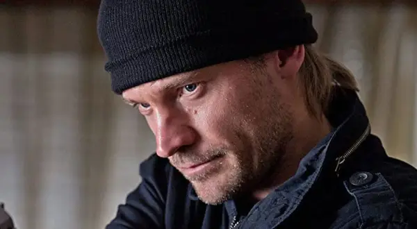 En man med svart mössa och skäggstubb, kanske en karaktär från filmer och tv-program med Jo Nesbø.