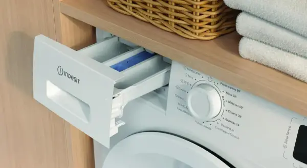 Szara szuflada na proszek w pralce Indesit, obok kosza z praniem. Instrukcja obsługi pomoże wybrać odpowiedni program.