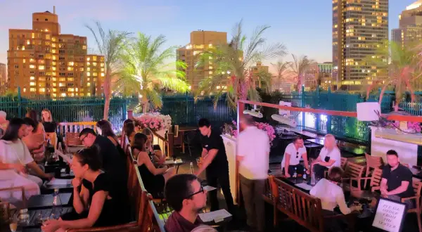 Un rooftop bar a New York City, con persone che si godono la vita notturna tra palme e luci della città.