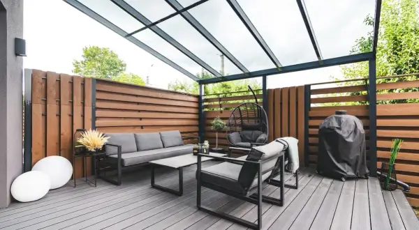 Arredamento moderno per un balcone con idee frangivista: divano, poltrone, dondolo e barbecue sotto una tettoia trasparente.