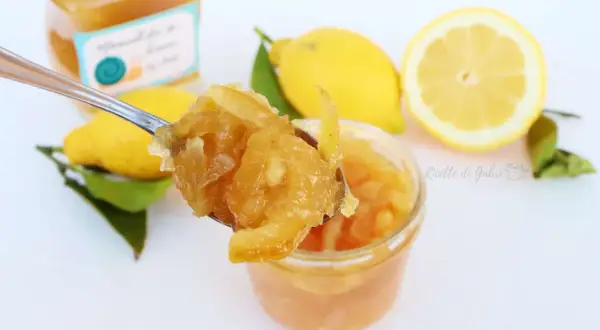 Un cucchiaio raccoglie la marmellata di limoni fatta in casa, con limoni freschi e foglie sullo sfondo.