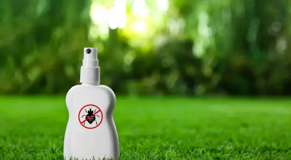 Biała butelka z atomizerem na trawie, z symbolem przekreślonego kleszcza. To produkt, czego nie lubią kleszcze.