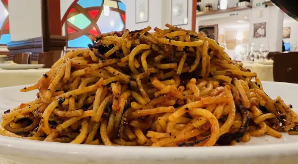 Un piatto di spaghetti con pomodoro e basilico, un classico del cibo barese, servito in un ristorante con vetrate colorate.