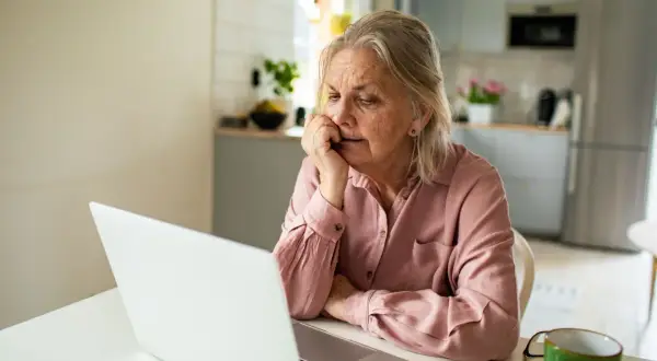 Femme âgée réfléchissant devant son ordinateur, cherchant des solutions pour savoir que faut il faire pour ne pas payer une maison de retraite.