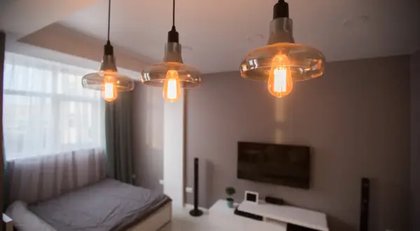Trzy lampy wiszące z żarówkami Edisona tworzą nastrojowe oświetlenie bez prądu, dodając ciepła wnętrzu sypialni z łóżkiem i telewizorem.