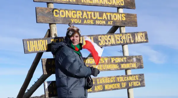 Zdobywca szczytu Kilimandżaro z polską flagą przy znaku "Uhuru Peak 5895m". Wyprawa na Kilimandżaro zakończona sukcesem!