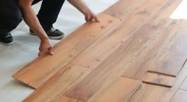 Hands installing laminate flooring. Is laminate flooring hard to install? This DIY project looks manageable.