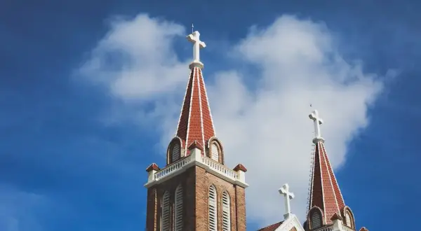 Dwie wieże kościelne z krzyżami na tle błękitnego nieba z chmurami. Czy kremacja jest grzechem? Pytanie to nurtuje wielu wiernych.