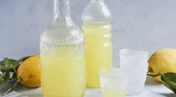 Ein Glas mit dem original italienischen Limoncello Rezept, daneben eine Karaffe, Flasche und Zitronen.