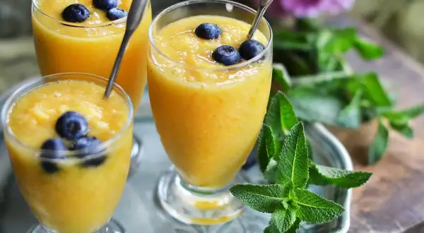 Tre glas med krämig mango smoothie, toppade med blåbär och mynta. En perfekt, uppfriskande dryck.