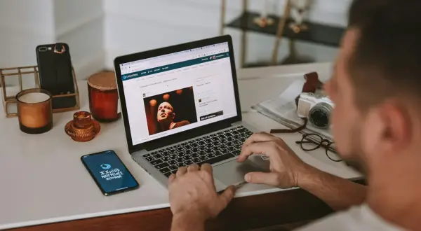 Mężczyzna przy biurku pracuje na laptopie, szukając informacji, jak sprawdzić model laptopa. Obok leży telefon i aparat.