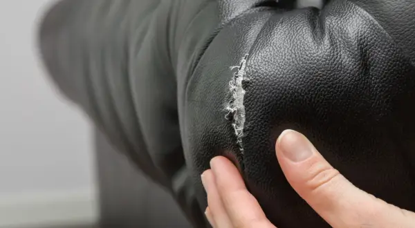 Main d'une personne examinant un accroc sur un fauteuil en cuir noir, montrant la nécessité de réparer le cuir craquelé.