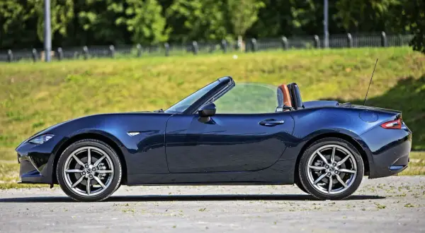 Granatowy roadster z otwartym dachem, gotowy na letnią przejażdżkę pośród zieleni.